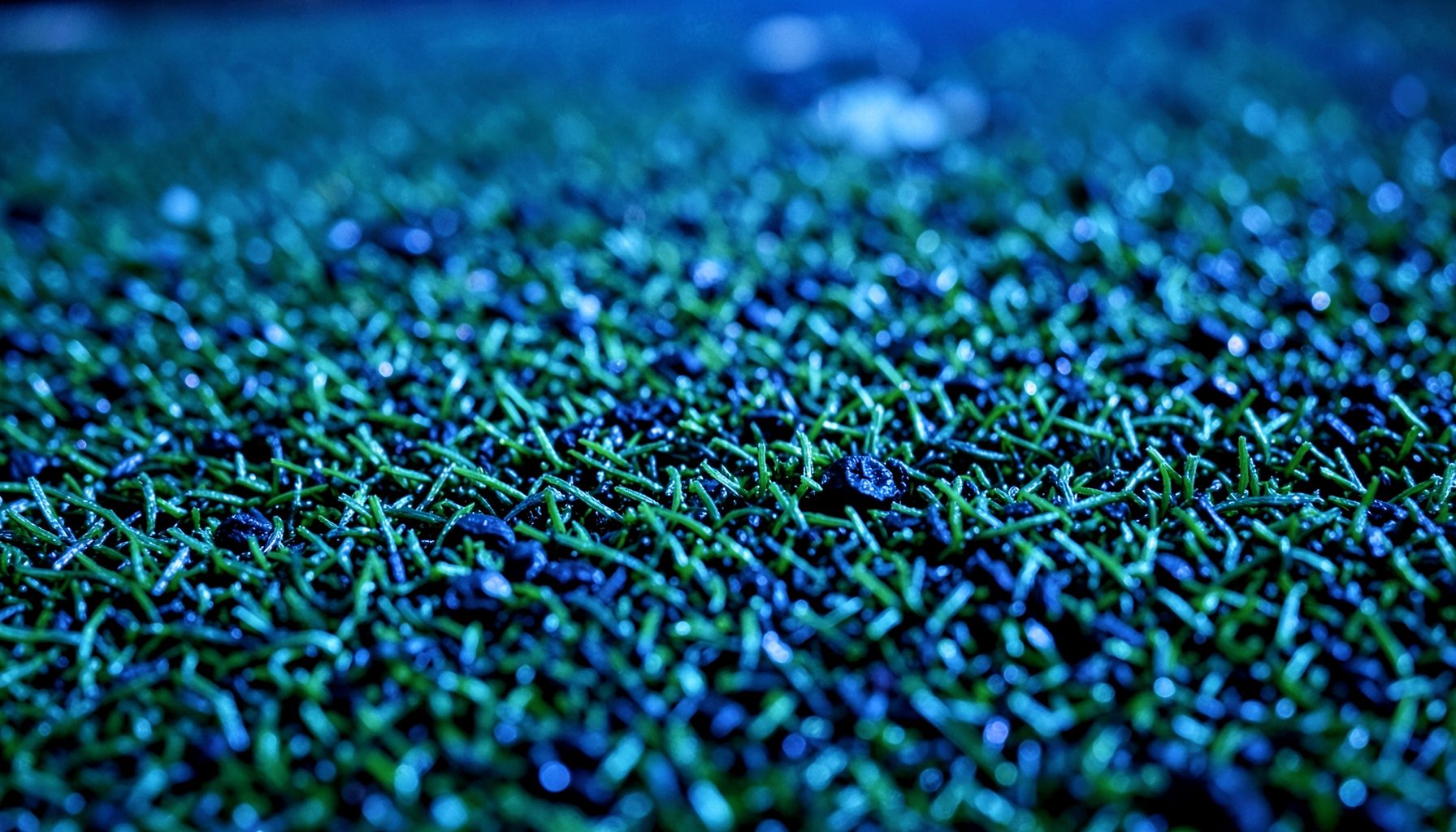Extreme close-up of a weathered football surface, deep green artificial turf fibers interspersed with dark rubber granules